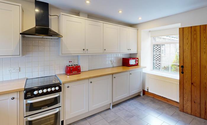 A clean, modern kitchen with integrated oven, bright red toaster and microwave, and views onto the cottage garden from a wide window.